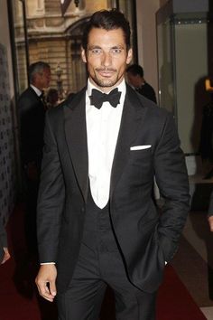 a man in a tuxedo and bow tie is walking down the red carpet