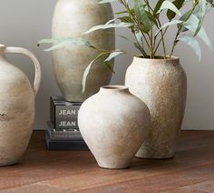 three white vases sitting on top of a wooden table next to a book and plant