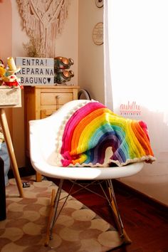 a white chair with a rainbow blanket on it's back in front of a window