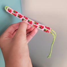 a hand holding a piece of string with red and green beads on it, in front of a blue wall