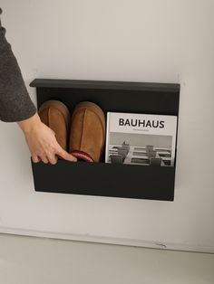 a person's hand pointing at a book in a shoe box on the wall