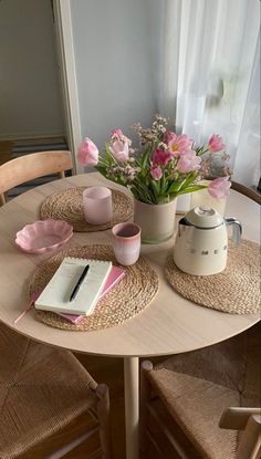 a wooden table topped with pink flowers next to a potted plant and a notebook