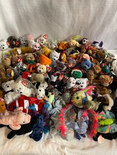 a pile of stuffed animals sitting on top of a white cloth covered bed spread in front of a white sheet