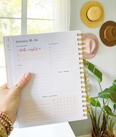 a woman is holding up a planner in her hand and pointing to it on the desk