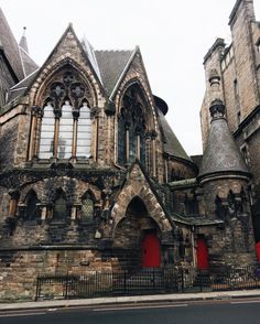 an old church with red doors and windows on the side of the street in front of two tall buildings