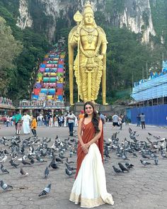 a woman standing in front of a statue with pigeons surrounding her and birds on the ground