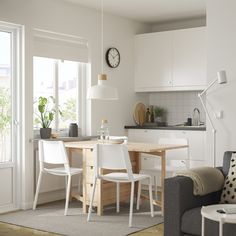 a living room and kitchen area with a couch, table, chairs and clock on the wall