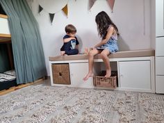 two young children sitting on top of a bed in a room with white walls and carpet