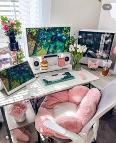 a desk with two computer monitors and pink pillows on it, along with other office supplies