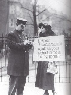 an old black and white photo of two people standing in front of a fence holding a sign