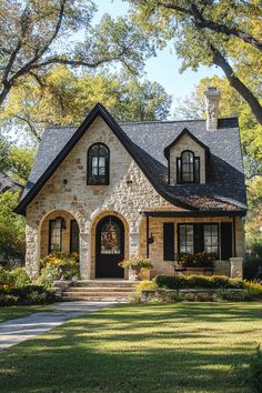 a stone house with black shutters on the front door and windows, surrounded by trees