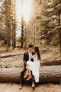 a bride and groom sitting on a log in the woods together for their engagement photos