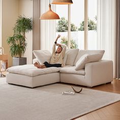 a man laying on top of a white couch in a living room next to a lamp