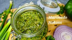 a jar filled with green sauce sitting on top of a wooden cutting board next to onions and celery