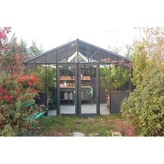 a small glass house sitting in the middle of a garden with lots of plants around it