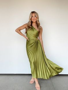 a woman standing in front of a white wall wearing a green dress with pleaed details