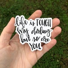 someone holding up a sticker that says life is tough my doing but so are you