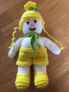 a crocheted snowman with yellow pants and green scarf on a wooden floor