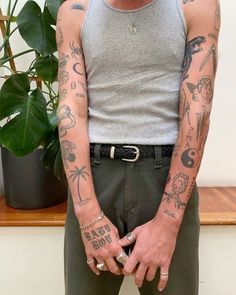 a man with many tattoos on his arm and chest standing in front of a potted plant