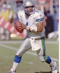 a football player holding a ball on top of a field with people in the background