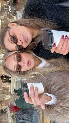 two beautiful young women standing next to each other holding coffee cups and looking at the camera