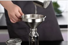 a person pours water into a cup from a metal strainer on top of a table