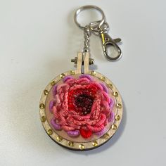 a pink and red flower on a wooden circle keychain with gold rivets