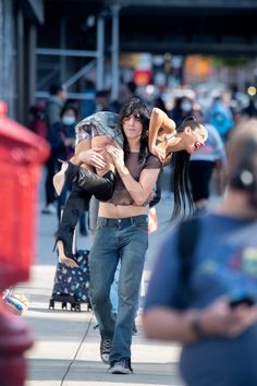 a man carrying a woman on his back while walking down the street with other people behind him