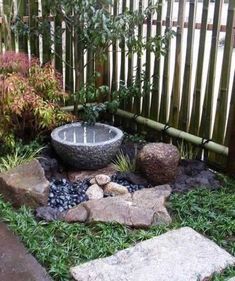 a small garden with rocks, grass and water feature in the center is surrounded by bamboo fencing