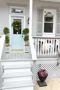 a white porch with flowers and potted plants on the steps next to the front door