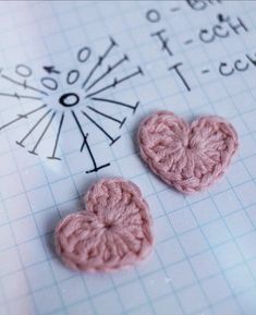 two pink crocheted hearts sitting on top of a piece of paper next to a ruler