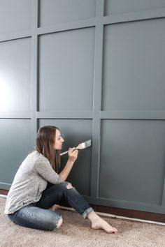 a woman is sitting on the floor with paint rollers in her hand and she is painting the wall