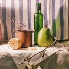 two pears and a green bottle sitting on a table next to a striped towel