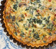 a quiche with spinach, mushrooms and cheese in a pie pan on a table