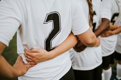 a group of people standing next to each other wearing white shirts with black numbers on them