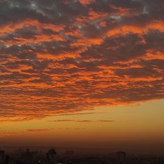 an orange sky with clouds and buildings in the background