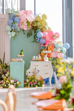 a room filled with lots of balloons and flowers on top of a white dresser next to a window