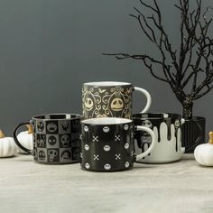 halloween themed coffee mugs sitting next to a small tree with spooky leaves