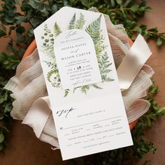 a close up of a wedding card on top of a flower pot with greenery