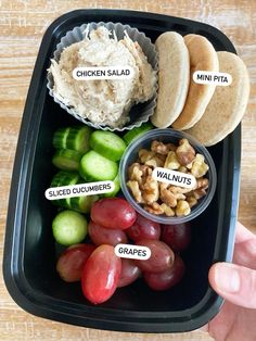 a black tray with grapes, crackers, hummus, walnuts and other food items