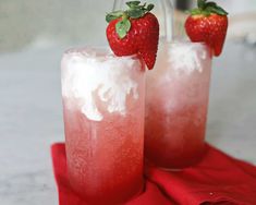 two glasses filled with ice and strawberries sitting on top of a red cloth next to each other