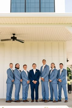 a group of men standing next to each other in front of a white building with a ceiling fan