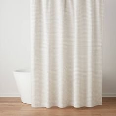 a white shower curtain hanging on the side of a bathtub in a room with wood floors