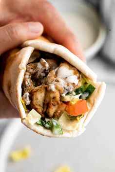 a hand holding a pita filled with meat and vegetables