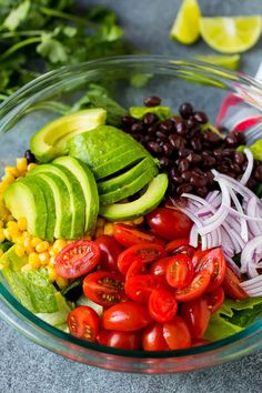 a glass bowl filled with vegetables, beans and avocado on top of a table