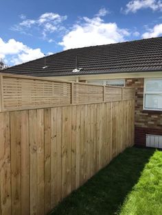 a wooden fence in front of a house with grass on the lawn and blue sky