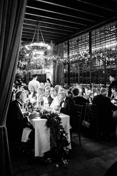 black and white photograph of people sitting at tables in a restaurant with chandeliers hanging from the ceiling