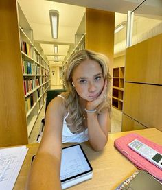 a woman sitting at a table with a tablet in front of her and bookshelves behind her