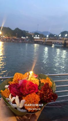 a person holding a bouquet of flowers in front of the water at night with lights on