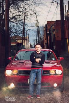 a man standing in front of a red car with his arms crossed and looking at the camera